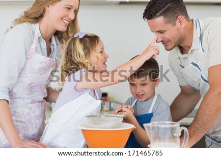 Playful girl touching nose of father while baking cookies with family in kitchen