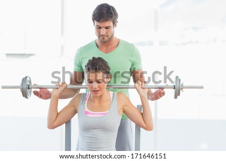 Male trainer helping young fit woman to lift the barbell bench press in the gym