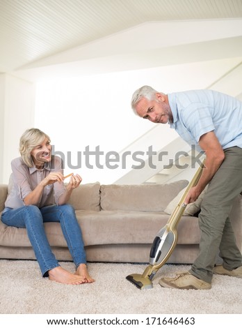 Woman filing nails while man using vacuum on area rug in the living room at home