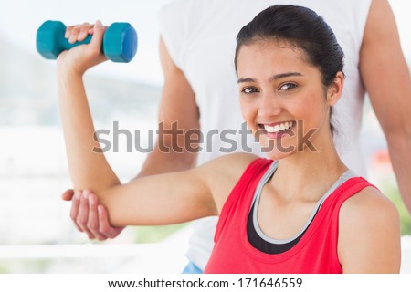 Close-up of an instructor assisting smiling woman with dumbbell weight in a bright gym