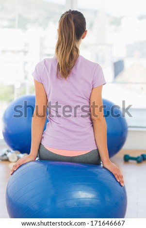 Rear view of a fit young woman sitting on exercise ball at a bright gym