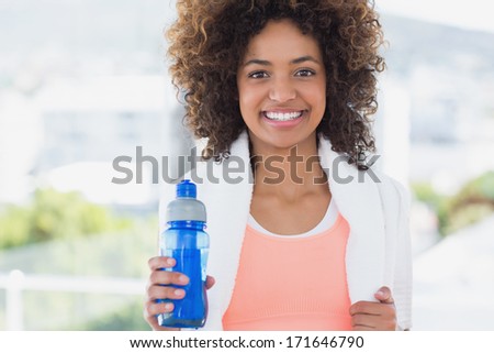 Portrait of a fit young female holding water bottle at a bright gym
