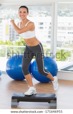 Full length of a fit young woman performing step aerobics exercise in ...