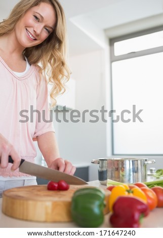 Portrait of happy young woman slicing vegetables on chopping board at kitchen counter