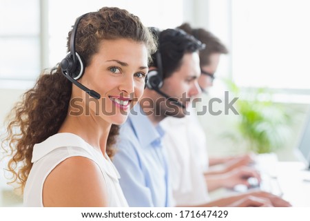 Portrait of young call center operator wearing headset with colleagues working in background at office