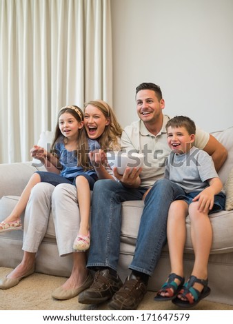 Full length of excited family watching television while sitting on sofa at home