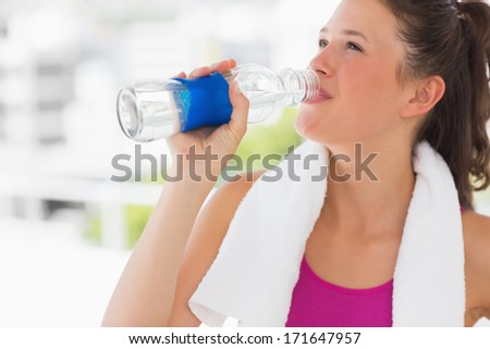Fit young woman with towel drinking water in the gym