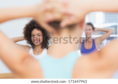 Close-up of smiling females with blurred trainer doing stretching exercises at fitness studio