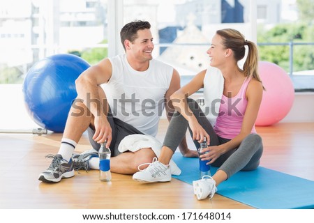 Young woman and man with water bottles chatting at a bright gym