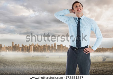 Thinking businessman with hand on head against large city on the horizon