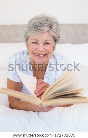 Portrait of happy senior woman turning story book pages in bed at home