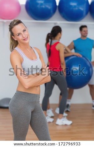 Portrait of a fit smiling young woman with friends in background at fitness studio