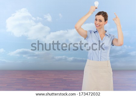 Classy businesswoman holding light bulb above her head against clouds in a room