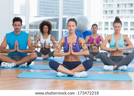 Sporty young people in Namaste position with eyes closed at a bright fitness studio