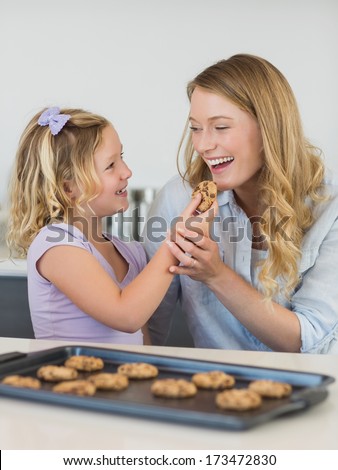 Smiling girl feeding cookie to mother in kitchen