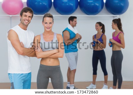 Portrait of a smiling couple with fitness class in background at gym