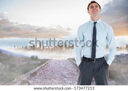 Smiling businessman standing with hand in pocket against rocky path leading to large urban sprawl