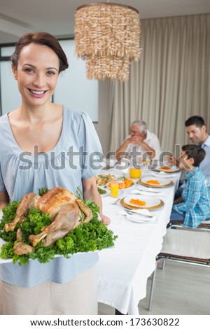 Portrait of a woman holding chicken roast with family at dining table in the house