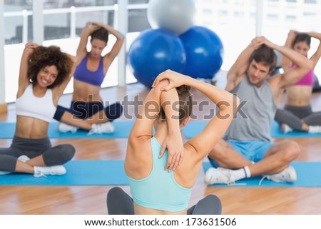 Young people with trainer stretching hands behind backs in a bright gym