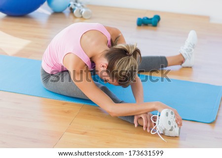 Full length of a sporty young woman stretching hand to leg in fitness studio