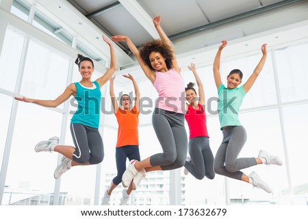 Full length portrait of fitness class and instructor jumping in fitness studio