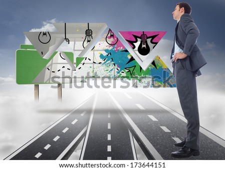 Serious businessman with hands on hips against roads over clouds with empty signposts