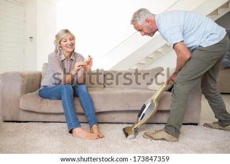 Woman filing nails while man using vacuum on area rug in the living room at home