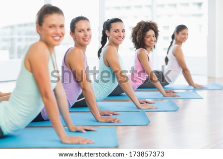 Side view portrait of a fit class doing the cobra pose in a bright fitness studio