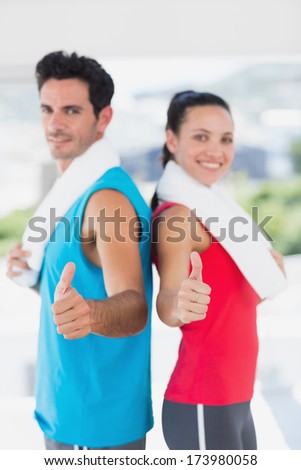 Portrait of a fit young couple gesturing thumbs up in a bright exercise room
