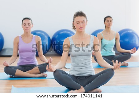 Sporty young women in meditation pose with eyes closed at fitness studio