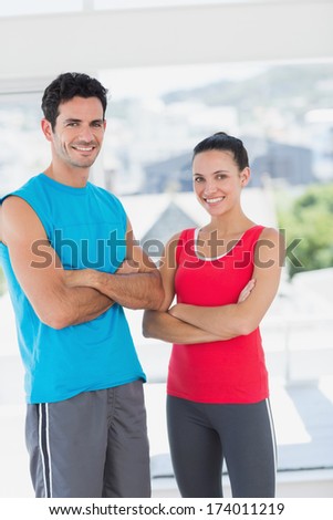 Portrait of a fit young couple standing with arms crossed in a bright exercise room