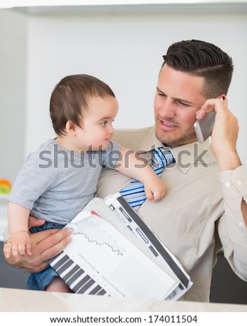 Irritated businessman carrying baby and documents while on call in kitchen