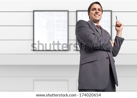 Thoughtful businessman holding pen against display in white room
