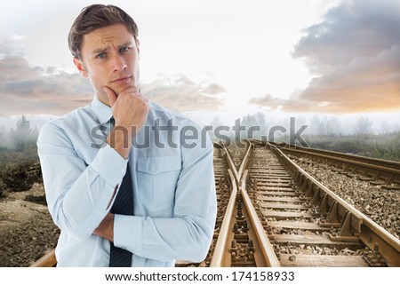 Thinking businessman with hand on chin against railway tracks leading to misty forest
