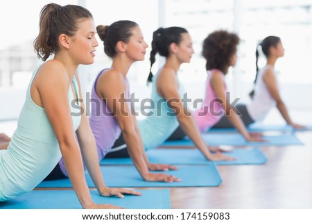 Side view of a fit class doing the cobra pose in a bright fitness studio