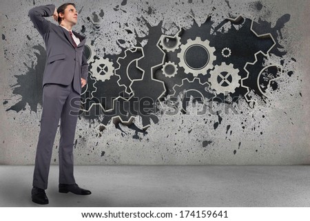Thinking businessman scratching head against splash on wall revealing cogs and wheels
