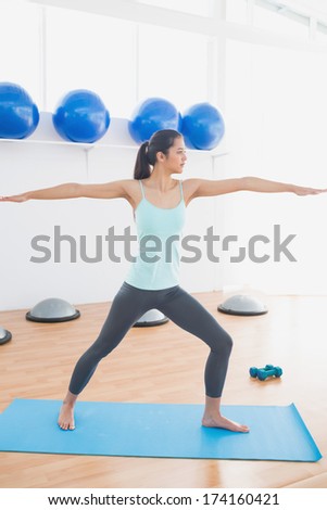 Full length of a sporty young woman stretching hands at yoga class in fitness studio