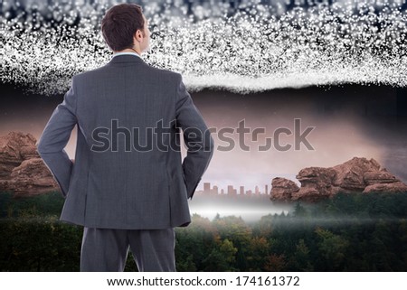 Businessman standing with hands on hips against bright stars of energy over landscape
