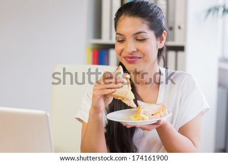 Young smiling businesswoman eating sandwich in lunch break at office