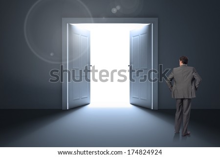 Businessman with hands on hips against doors opening revealing light