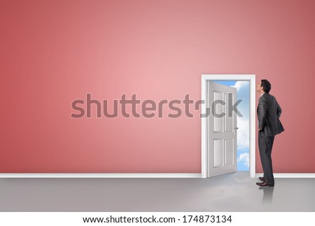 Smiling businessman with hands on hips against door opening showing blue sky