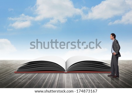 Smiling businessman with hands on hips against open book against sky