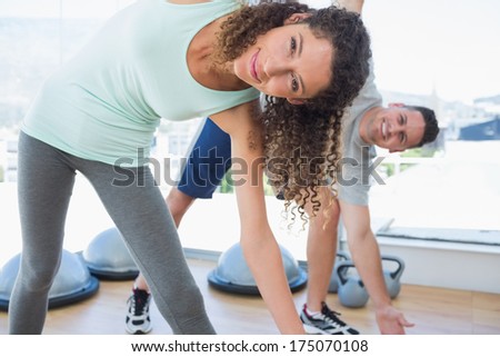 Portrait of fit woman with man doing stretching exercise at gym