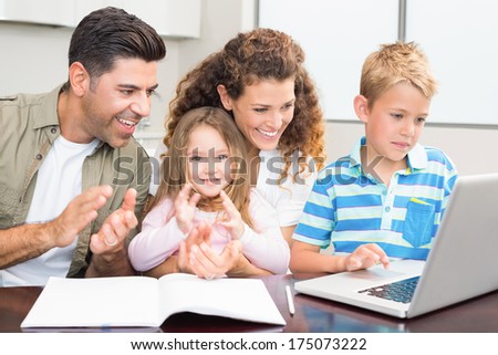 Happy parents using laptop with their young children at home in kitchen