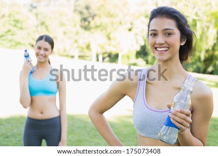 Portrait of beautiful sporty woman holding water bottle with friend in background