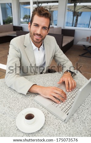 Smiling businessman working with his laptop at table having coffee in patio of restaurant