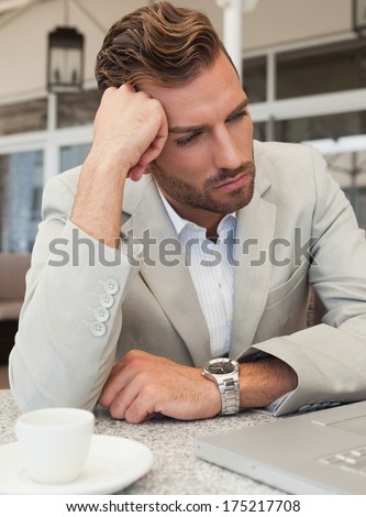 Frowning businessman looking at his laptop in patio of restaurant