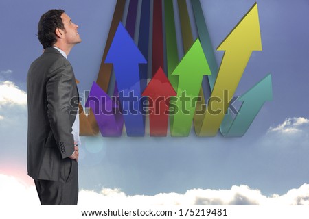 Smiling businessman with hand on hip against colourful arrows pointing up against sky