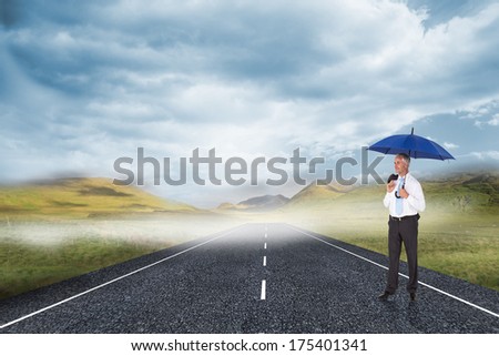 Happy businessman holding umbrella against cloudy landscape background with street