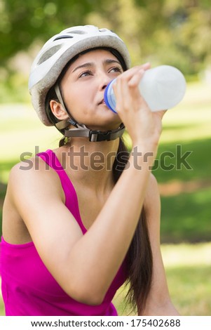 Close-up of a fit young woman in helmet drinking water at the park